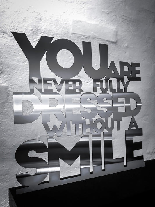 You are never fully dressed without a smile - Rustfri stål 52,5x50cm